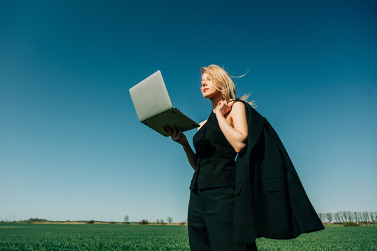 Businesswoman holding laptop in a green wheat field