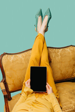 Person relaxing on a vintage sofa holding a blank digital tablet