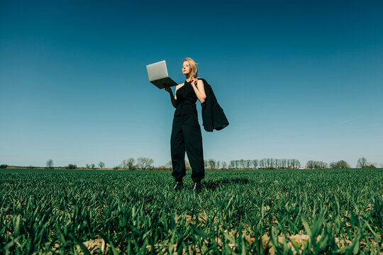 Businesswoman holding laptop in green field under blue sky