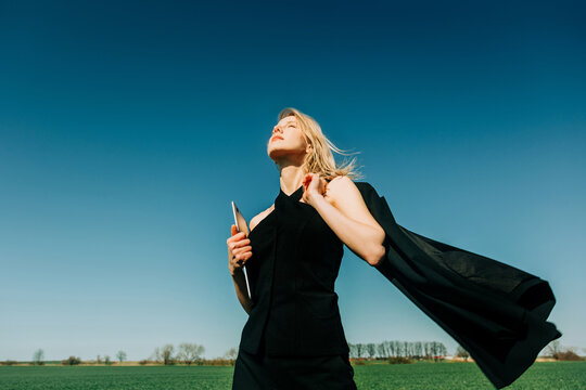 Businesswoman holding laptop in a green wheat field expressing freedom
