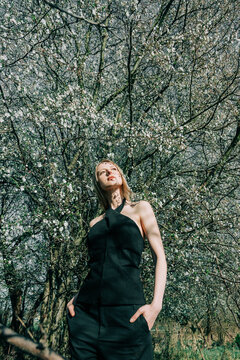 Stylish fashion model standing under spring blossom tree