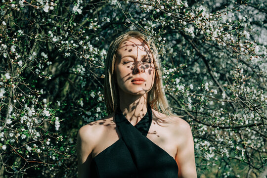 Stylish portrait of a woman with eyes closed under spring blossom tree