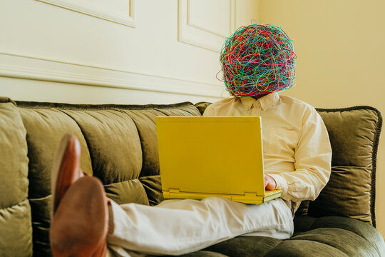 Businessman wearing mask of chaotic thoughts and working on laptop
