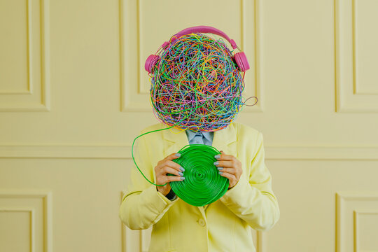 Woman with mask of chaotic thoughts holding spiral roll in front of wall