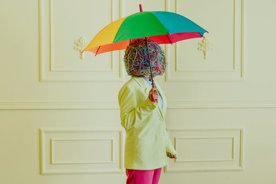 Woman with mask of chaotic thoughts standing under colorful umbrella