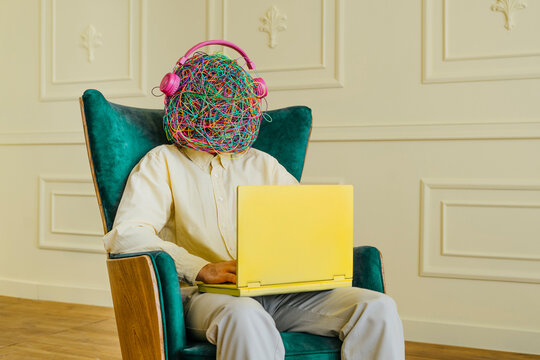Man with mask of chaotic thoughts listening to music and using laptop