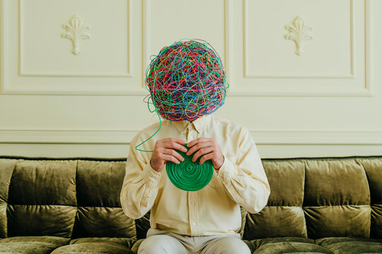 Man with mask of chaotic thoughts solving tangled wires