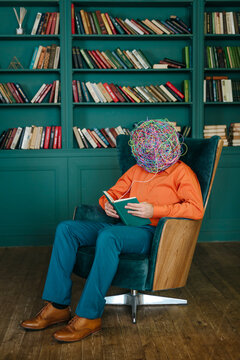Man with mask of chaotic thoughts sitting on chair and reading book