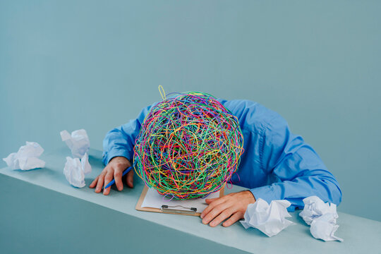 Frustrated businessman with mask of chaotic thoughts amidst crumpled paper