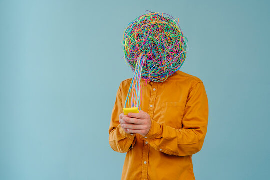 Man with mask of chaotic thoughts using smart phone against blue background