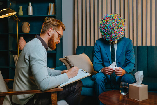 Psychotherapist writing problems of worried patient sitting on sofa