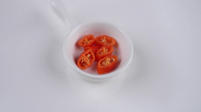 Rotating Sliced Chili in Small White Handled Bowl Isolated on White Background for Spicy Ingredient Presentation Concept