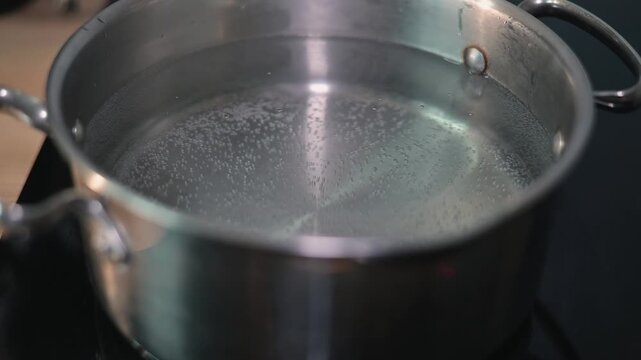 A pot filled with water sits on a stove as bubbles begin to form and rise, indicating it is heating up