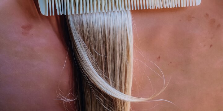 Muted rose brown background behind silky blonde hair flowing through a white comb for beauty salon brochures, haircare product marketing and editorial hair styling