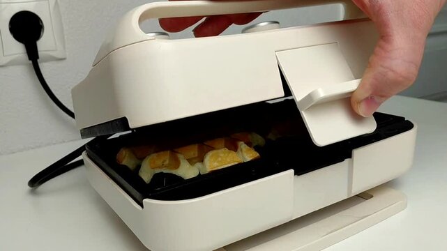 The process of making homemade Belgian (Viennese) waffles. A man's hand closes an electric waffle iron with homemade waffle dough.