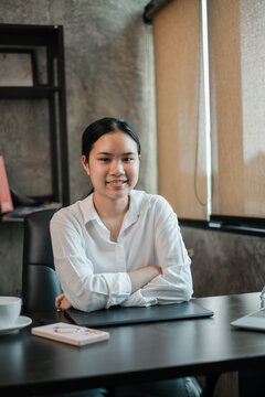 Young woman in a modern office, seated at a desk with a confident smile, surrounded by contemporary decor and natural lighting.