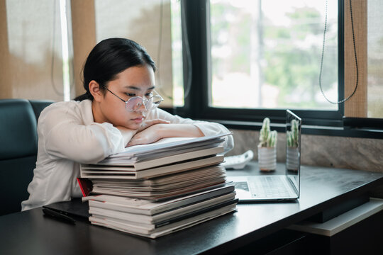 Focused young woman in glasses studying with a laptop and books in a modern office environment.