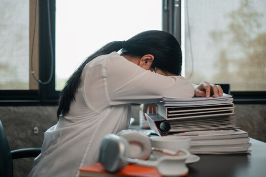 Tired employee resting on a pile of paperwork at a desk, illustrating workplace stress and fatigue.