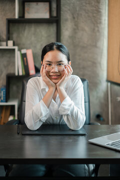 Confident woman in glasses sitting at desk in a modern office environment, showcasing a professional work atmosphere.