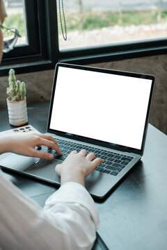 Individual working on a laptop with a blank screen in a cozy, well-lit workspace featuring a small cactus plant.
