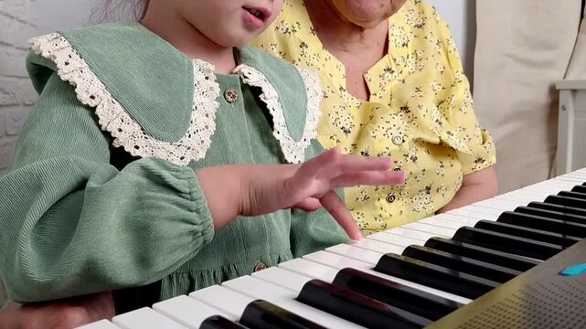 Elderly grandmother teaching little sweet girl playing piano, smiling with happiness, staying at cozy home, spending time together. Family, Love, Education Concept.