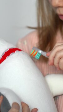 Close up of little girl brushes teeth of toy shark with toothbrush. Oral hygiene. Health care. Vertical shot