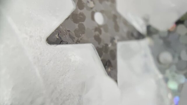 Macro abstract video of silver star sequins frozen in ice with dreamy blur and shimmering reflections, ideal for winter and luxury visuals.