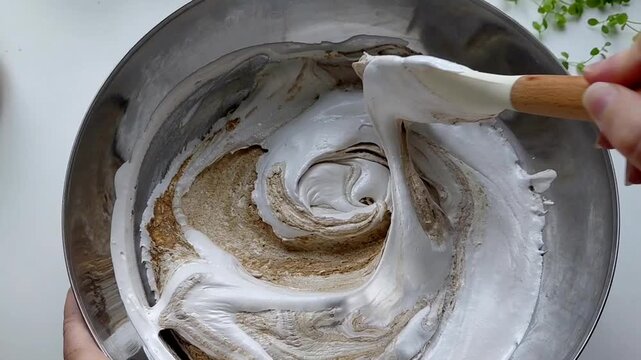 A person kneads the halva ingredients in a bowl with a spatula, preparing it. Various ingredients are visible in the finished mixture. Sunflower halva.