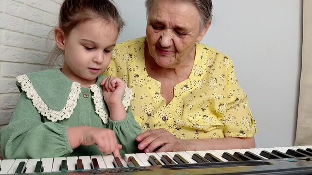 Elderly grandmother teaching little sweet girl playing piano, smiling with happiness, staying at cozy home, spending time together. Family, Love, Education Concept.