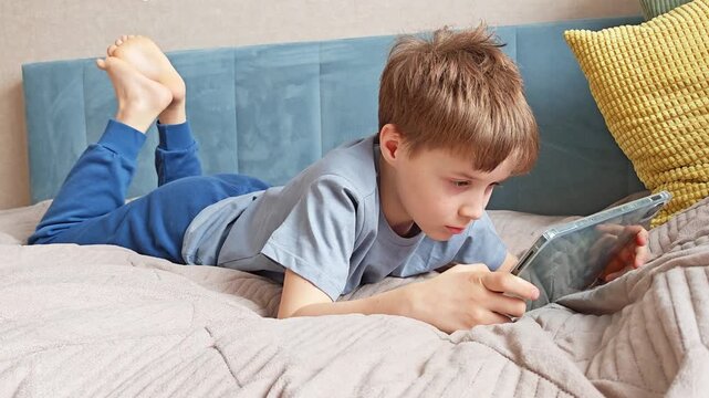 Boy lying on sofa playing game on tablet. relaxed posture, home leisure, digital entertainment, childhood fun.
