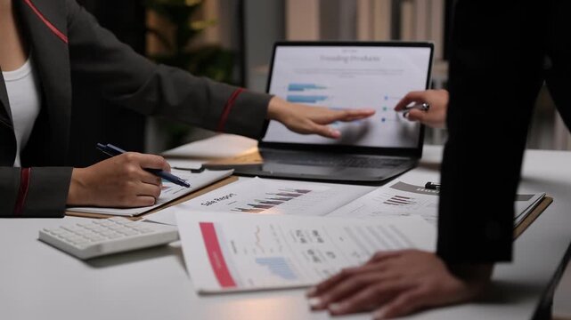 Business colleagues collaborating on a financial report in the office. Business team analyzing financial data on a laptop and documents. Colleagues discussing a marketing strategy and company growth.