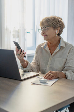 Smiling senior woman using laptop and smartphone at home for online banking or bill payment