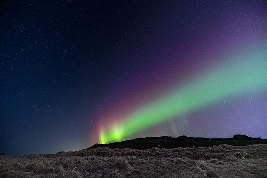 View of ethereal aurora borealis dances across the dark sky, casting vibrant green and purple hues over the serene landscape, Krysuvikurkirkja, Iceland.