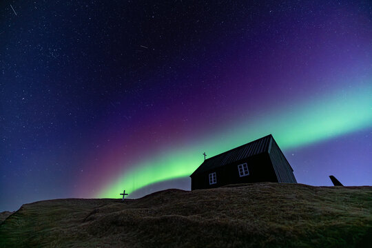 View of the silhouetted Krysuvikurkirkja church stands peacefully under the vibrant, dancing green and purple hues of the northern lights, Krysuvikurkirkja, Hafnarfjardarkaupstadur, Iceland.
