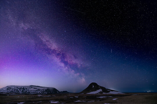 View of the Milky Way's ethereal glow painting the Icelandic night sky above dark, rugged mountains, a stunning vista of cosmic beauty, Krysuvikurkirkja, Iceland.