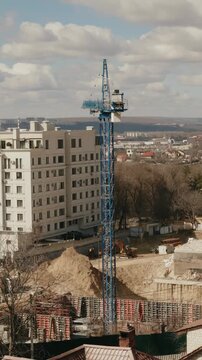 Industrial tower crane operating on a new building construction site, moving materials and machinery across the foundation works with a cloudy urban landscape in the city. timelapse. vertical