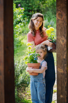 Happy mother and daughter with yellow dahlias on wooden terrace in summer garden.