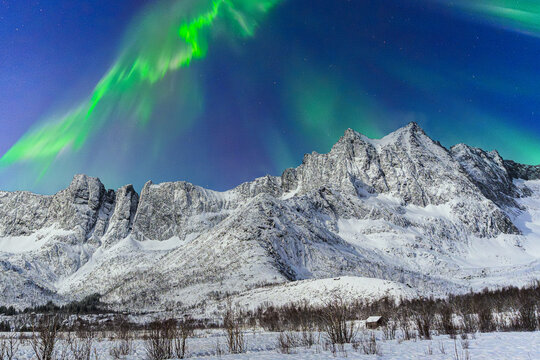 View of dazzling green aurora borealis over rugged, snow-capped mountains and a serene winter landscape, Mefjordvaer, Troms, Norway.