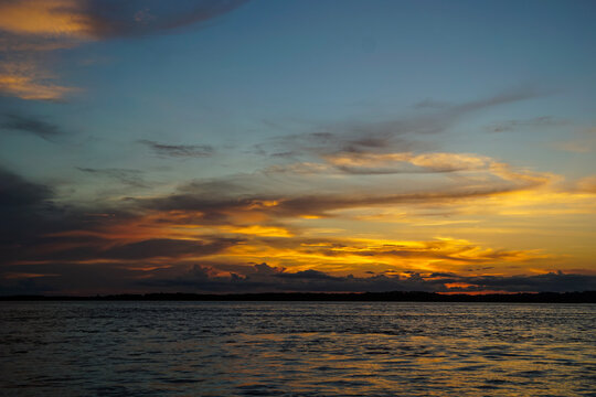 A serene sunset over an amazon river in Peru, featuring a vibrant orange and yellow sky reflecting on the calm surface.