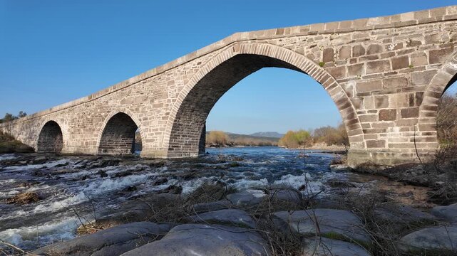 Ancient Stone Bridge over Tuzla Stream near Assos, Behramkale, Turkey Historical Ottoman Architecture and River Landscape at Sunset. High quality 4k footage