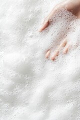 Fototapeta premium Hand submerged in white sudsy water with many small bubbles, close-up view.