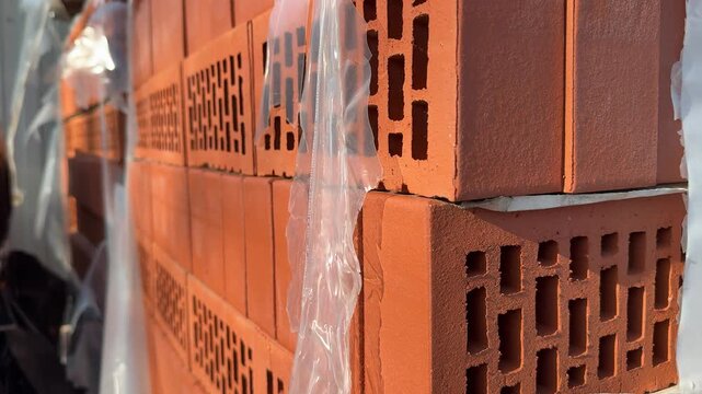 Close-up stacked red bricks hardware store, street side pallet of hollow clay blocks wrapped in plastic, sunlight highlighting rough.