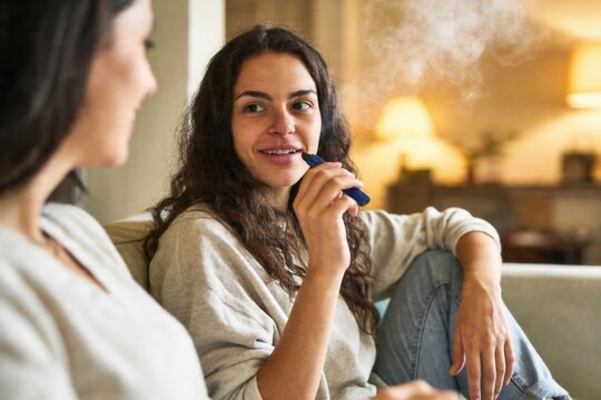 Woman using a vape pen, exhaling smoke while relaxing and talking with friend