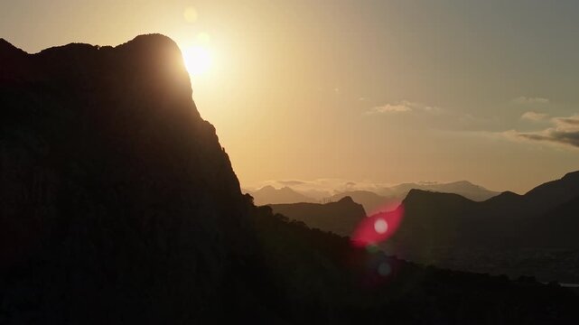 Sunrise over Penon de Ifach cliff with mountain silhouettes and golden sky aerial view Calpe Spain