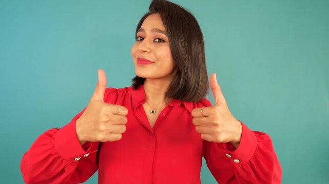 Closeup portrait of happy positive beautiful young woman looking at camera showing thumbs up hands gesture sign well-done like recommend good, isolated over blue studio background.