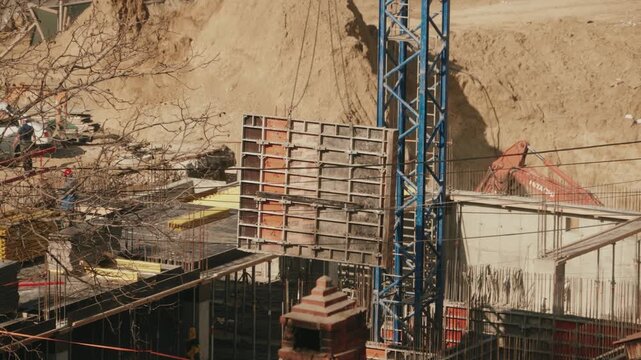 High angle view of a tower crane maneuvering a large concrete formwork panel over the foundation pit of a new building, illustrating the early stages of structural development on the site