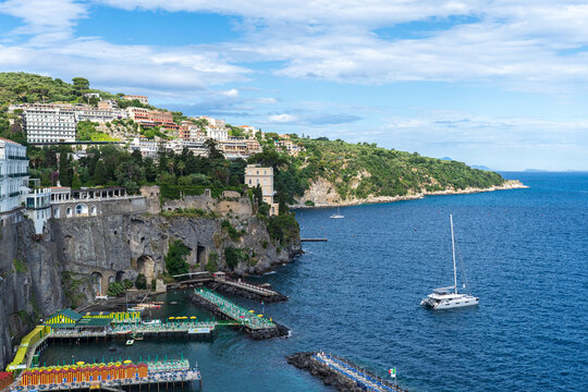 View of the azure sea meeting the rugged cliffs, dotted with buildings and boats, creating a vibrant coastal scene, Sorrento, Campania, Italy.