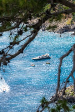 View of a luxurious yacht and small boats resting on the shimmering blue waters framed by lush greenery, Capri, Campania, Italy.