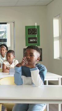 Vertical video: Hearing voice from right, boy in blue shirt turning at school desk, MATH poster