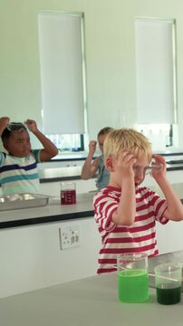 Vertical video: Picking item blond boy red tee donning goggles in lab for safety, viewing green cyl